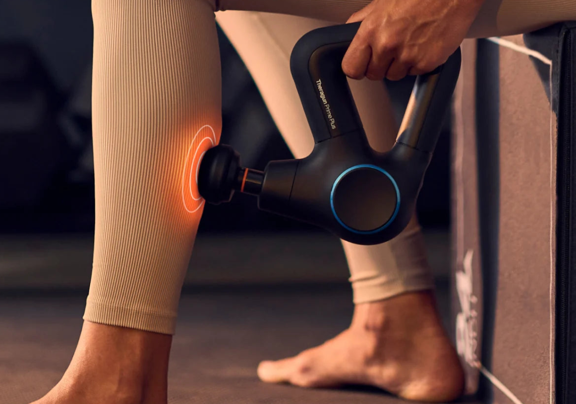 Kvinna använder en massagepistol - Theragun Prime Plus - med vibrations-massage på ett gym