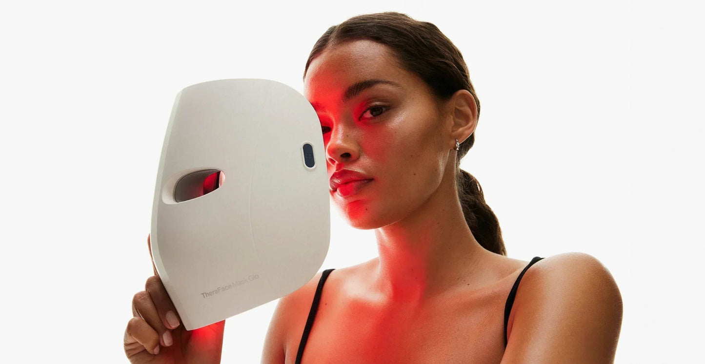 Woman holding a LED face mask with red light on a white background